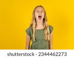 Caucasian kid girl wearing green T-shirt over yellow background angry and mad screaming frustrated and furious, shouting with anger. Rage and aggressive concept.