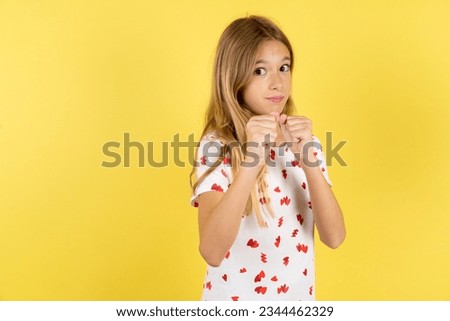 Caucasian kid girl wearing polka dot shirt over yellow background Ready to fight with fist defense gesture, angry and upset face, afraid of problem.