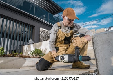 Caucasian Landscaper Drilling Holes Using Professional Cordless Driller Inside Concrete Backyard Elements For LED Lighting Installation. Outdoor Stairs Illumination.