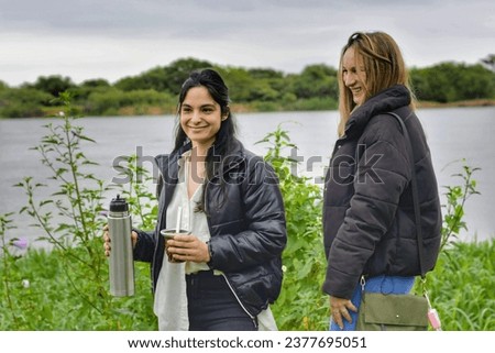 Caucasian latin girls walk along the banks of the river while drinking mate.