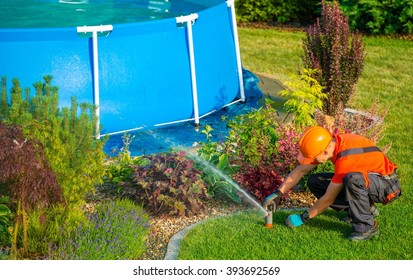 Caucasian Lawn Garden Technician In The Residential Garden With Swimming Pool Taking Care Of Lawn Sprinklers System.