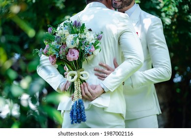 caucasian LGBTQ gay couple wearing white suit,standing outdoor, hugging together with holding flowers bouquet in wedding ceremony and celebration. Concept,selective focus. - Powered by Shutterstock