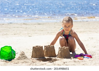 Caucasian little girl of five years old in swimsuit on sand beach and made forms and castles from sand