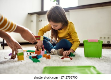 Caucasian little girl spending time with african american baby sitter, playing with construction toys set, sitting on the floor. Leisure activities, babysitting concept. Horizontal shot