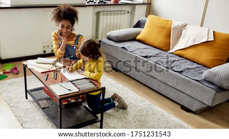 Caucasian little girl spending time with african american baby sitter. They are drawing, learning to write letters, sitting on the floor. Children education, leisure activities, babysitting concept