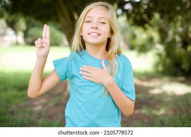 caucasian little girl wearing blue t-shirt standing outdoors smiling swearing with hand on chest and fingers up, making a loyalty promise oath.