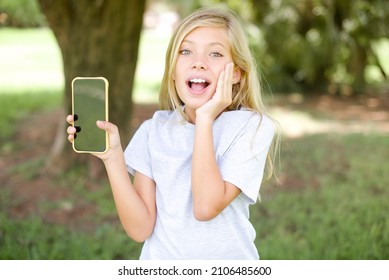 Caucasian Little Kid Girl Wearing T-shirt Standing Outdoors Hold Hand Modern Technology Use Touch Face Palm Astonished Impressed Scream Wow Omg Unbelievable Unexpected