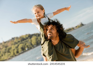 Caucasian loving father with happy daughter on shoulders walking on the beach. Loving father holding little kid child piggyback on weekend along lake river - Powered by Shutterstock