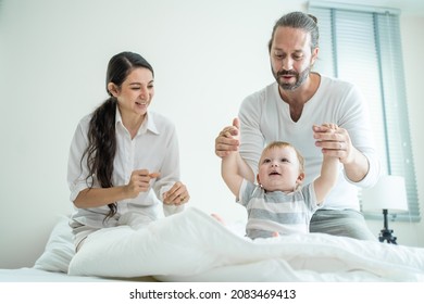 Caucasian Loving Parents Play With Baby Boy Child On Bed In Bedroom. Happy Family, Attractive Beautiful Young Couple Dad And Mom Dance With Cute Infant Toddler Son Enjoy Morning Activity After Wake Up