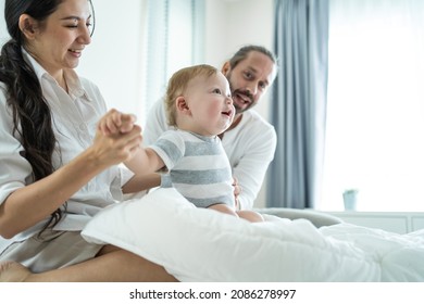 Caucasian Loving Parents Play With Baby Boy Child On Bed In Bedroom. Happy Family, Attractive Beautiful Young Couple Dad And Mom Dance With Cute Infant Toddler Son Enjoy Morning Activity After Wake Up