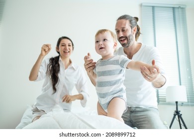 Caucasian Loving Parents Play With Baby Boy Child On Bed In Bedroom. Happy Family, Attractive Beautiful Young Couple Dad And Mom Dance With Cute Infant Toddler Son Enjoy Morning Activity After Wake Up