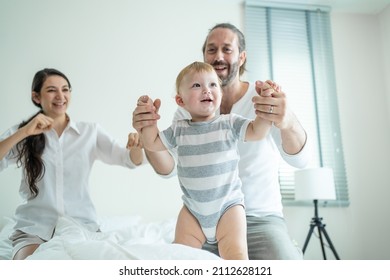 Caucasian Loving Parents Play With Baby Boy Child On Bed In Bedroom. Happy Family, Attractive Beautiful Young Couple Dad And Mom Dance With Cute Infant Toddler Son Enjoy Morning Activity After Wake Up