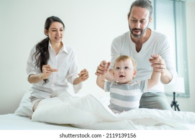 Caucasian Loving Parents Play With Baby Boy Child On Bed In Bedroom. Happy Family, Attractive Beautiful Young Couple Dad And Mom Dance With Cute Infant Toddler Son Enjoy Morning Activity After Wake Up