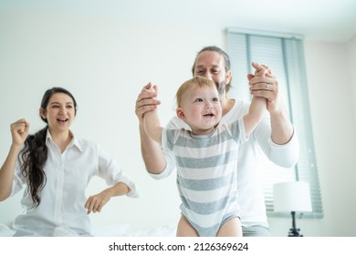 Caucasian Loving Parents Play With Baby Boy Child On Bed In Bedroom. Happy Family, Attractive Beautiful Young Couple Dad And Mom Dance With Cute Infant Toddler Son Enjoy Morning Activity After Wake Up