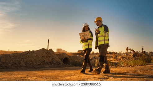 Caucasian Male Architect And Hispanic Female Urban Planner Walking On Construction Site With Laptop Computer And Talking About New Real Estate Project. Construction Equipment Working. Golden Hour - Powered by Shutterstock