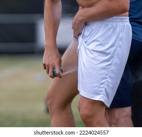 A Caucasian Male Athlete Self Treats A Groin Strain With Painkilling Analgesic Spray Directing A Jet Of Freezing Cold Liquid Mist Up The Leg Of His White Shorts. 