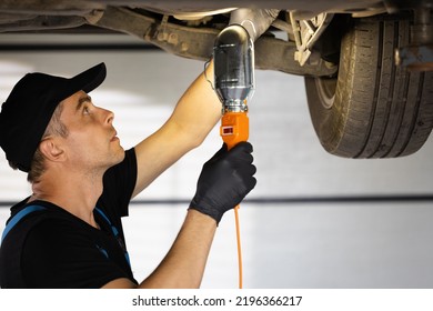 Caucasian Male Car Mechanic Checking Car. Auto Mechanic Working Underneath Car Lifting Machine At The Garage. Working In Car Repair Shop And Running Small Feminine Business Concept.