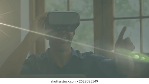 Caucasian male chef wearing virtual reality headset, pointing. Sunlight streaming through window, creating lens flare. Middle-aged man has short gray hair, wearing dark shirt, experiencing VR - Powered by Shutterstock