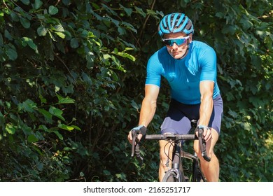 Caucasian Male Cyclist With Professional Racing Sports Gear Riding On An Open Road Cycling Route Through A Forest