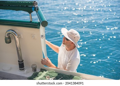 Caucasian Male Deckhand Engineer doing maintenance work on a superyacht with a wide brim hat and blue sea in the background and 