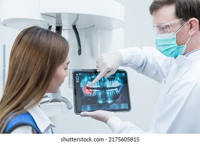 Caucasian male dentist hold digital tablet and explaining tooth problem. Caucasian male doctor use tablet and giving advice or consultation to Asian young girl patient about oral care in dental clinic