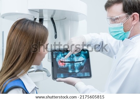 Caucasian male dentist hold digital tablet and explaining tooth problem. Caucasian male doctor use tablet and giving advice or consultation to Asian young girl patient about oral care in dental clinic
