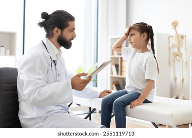 Caucasian male doctor examines young girl with headache on medical couch. Doctor dressed in white coat holds tablet with child patient. Scene in medical office exudes care and professionalism. - Powered by Shutterstock