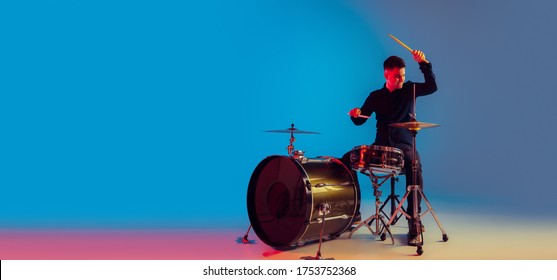 Caucasian male drummer improvising isolated on blue studio background in neon light. Performing, looks inspired, energy. Concept of human emotions, facial expression, ad, music, art, festival. Flyer.