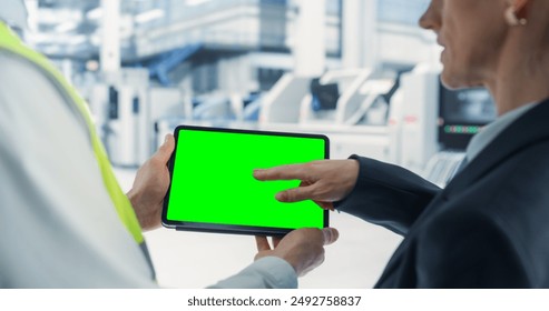 Caucasian Male Engineer Using Tablet With Green Screen Chromakey on Display And Talking To Female Supervisor At Autonomous Assembly Line At an Electronics Factory. Colleagues Discussing New Projects. - Powered by Shutterstock