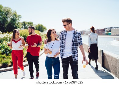 Caucasian Male And Female Friends Walking At City Embankment Enjoying Live Meeting For Communicate, Happy Hipster Guys With Non Alcohol Cocktails To Go Spending Leisure Weekend Togetherness