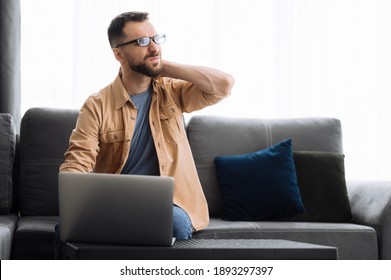 Caucasian Male Freelancer Guy Sits On The Couch At Home, Using Laptop. Tired Programmer Develop A Project, Have A Back Ache, Needing A Rest Or Break