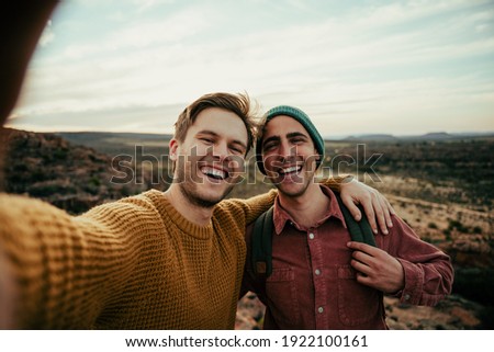 Caucasian male friends hiking in wilderness taking selfie with cellular device embracing the outdoors