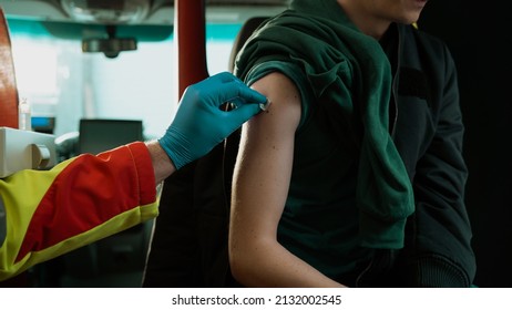 Caucasian Male Getting A Vaccine Shot In His Arm Sitting In The Ambulance Car, While The EMS Worker Holds A Cotton To Stop The Bleeding.