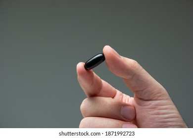 Caucasian male hand holding a black medicine capsule pill between fingers close up shot isolated studio shot.
