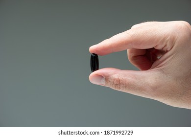 Caucasian male hand holding a black medicine capsule pill between fingers close up shot isolated studio shot.