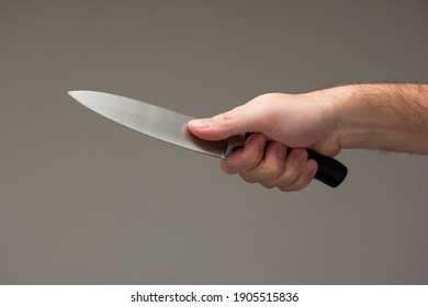 Caucasian male hand holding a large kitchen knife isolated on gray background.
