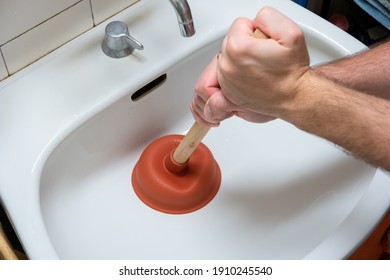 Caucasian male hand holding a plunger unclogging a bathroom sink.
