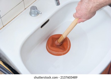 Caucasian male hand holding a plunger unclogging a bathroom sink.