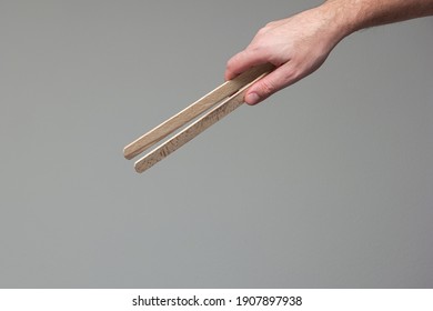 Caucasian male hand holding a wooden tong close up shot isolated on gray background.