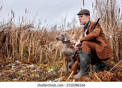 caucasian male hunter in suit clothes ready to hunt, holding gun and walking in forest. hunting and people concept. confident male in hat sit with dog waiting for prey animal. companion dog