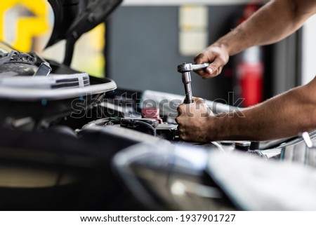 Caucasian male mechanic repairs car in garage. Car maintenance and auto service garage concept. Closeup hand and spanner.