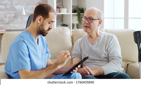Caucasian male nurse talking with a nursing home patient about his health. The nurse is making notes on a digital tablet