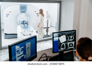 Caucasian male patient undergoing CT scan procedure while female technician supervises. Medical professionals examining diagnostic images on monitors in hospital setting, technology and healthcare. - Powered by Shutterstock