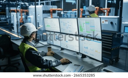Caucasian Male Process Engineer Using Multi Monitor Workstation To Control Production Of Modern Heavy Machinery on Autonomous Assembly Line With Robotic Arms. Man Adjusting Manufacturing Processes.