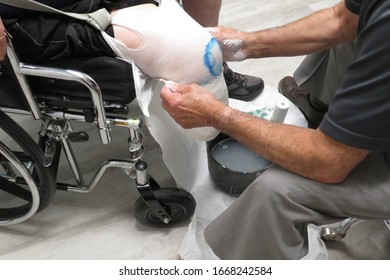 A Caucasian Male Prosthetist Wraps Gauze And Plaster Around The Residual Limb Of An Amputee In A Wheelchair To Fit Him For An Artificial Leg (limb)