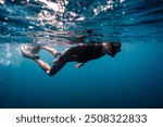 Caucasian Male snorkeler swimming in deep blue waters with mask,snorkel, fins and black rash guard swimming gear