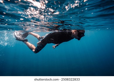 Caucasian Male snorkeler swimming in deep blue waters with mask,snorkel, fins and black rash guard swimming gear