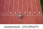 Caucasian male sprint runner alone on the athletic track, taking starting position and running in line four, aerial above shot.