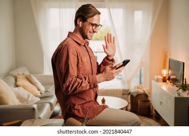 Caucasian Male Student Working From Home Holding Cellular Device Waving To Camera