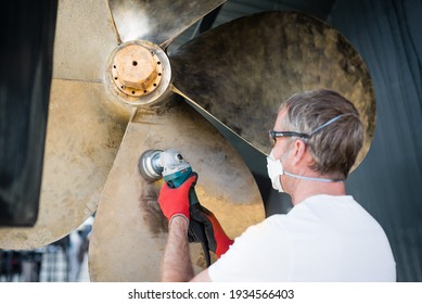 Caucasian male superyacht deckhand engineer polishing a yacht propeller with a power tool, gloves, mask and eye protection glasses 